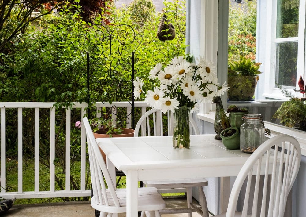 Varanda aconchegante com móveis brancos e margaridas
