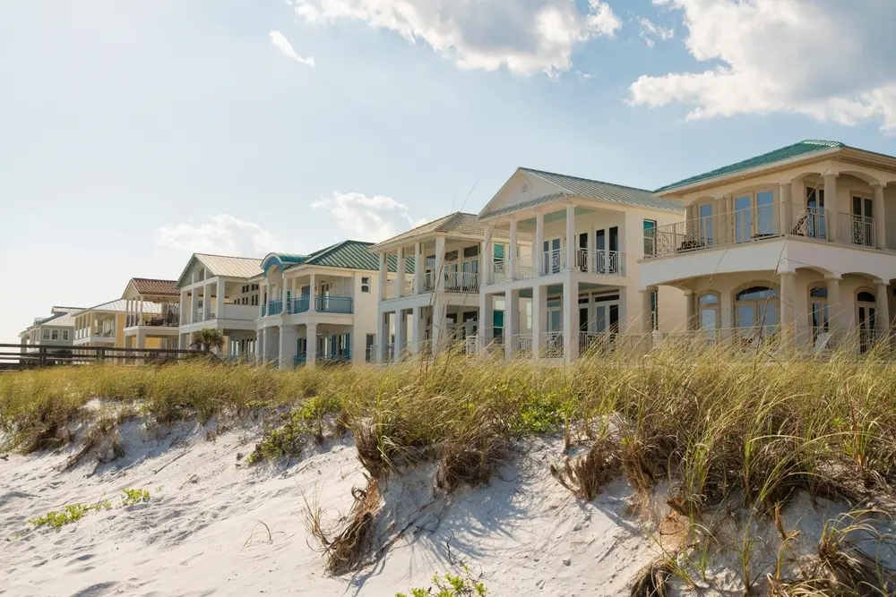 White sand dunes with grasses at the front of three-storey houses at the beach.