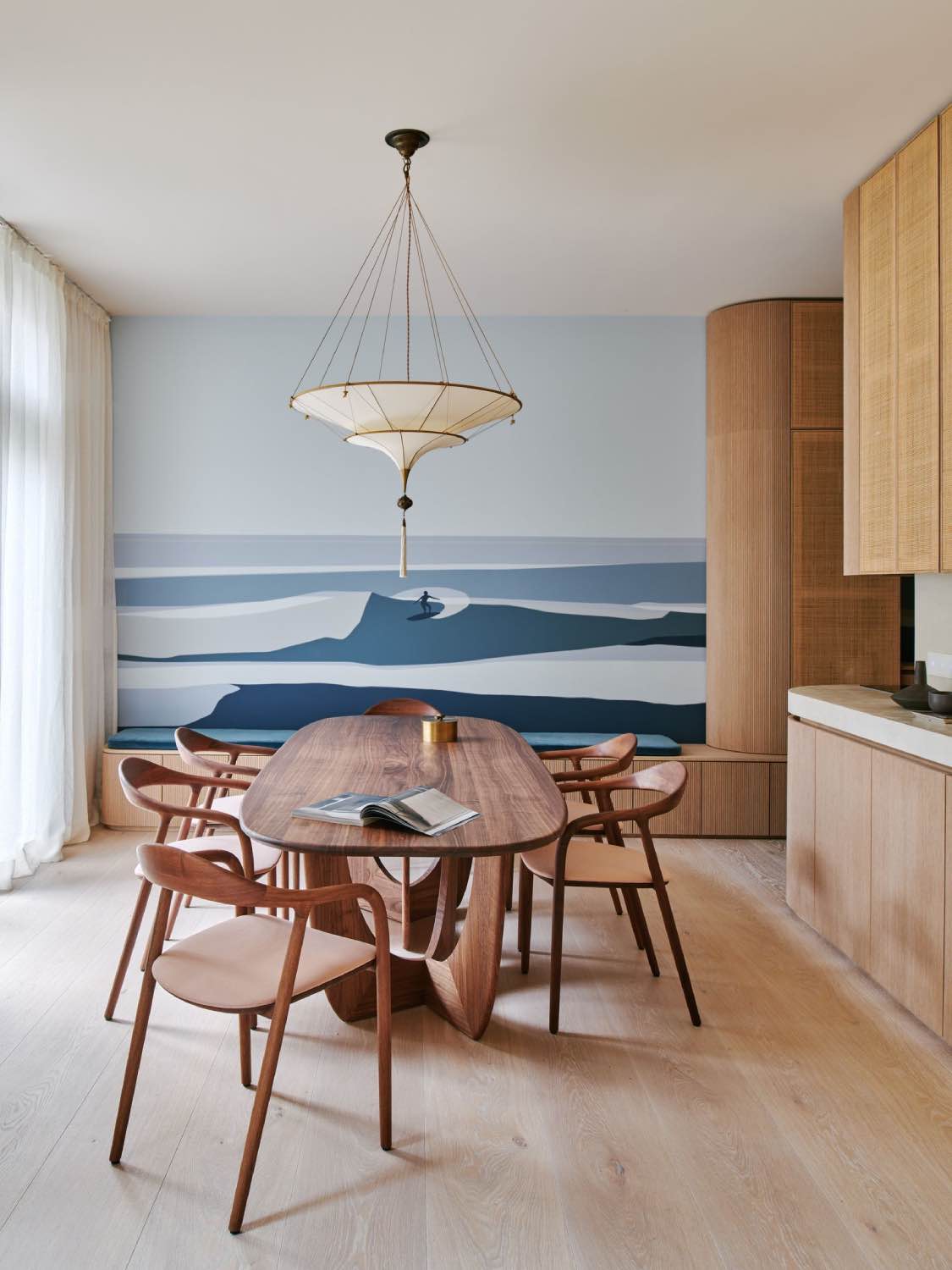 comedor de madera con mesa escultural y sillas, pared con mural