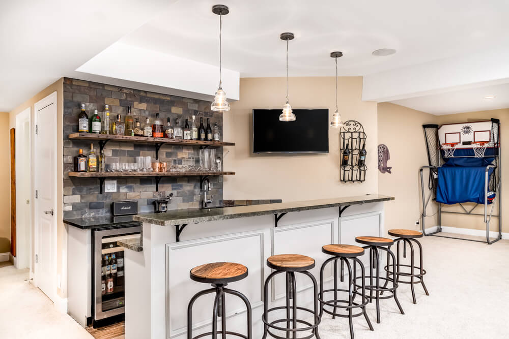 A small basement bar /man cave with liquor on shelves and the bar is surrounded by wood bar stools.
