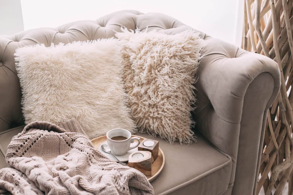 Coffee and sweater on the sofa with fur cushions. Cozy winter scene in Scandinavian interior.