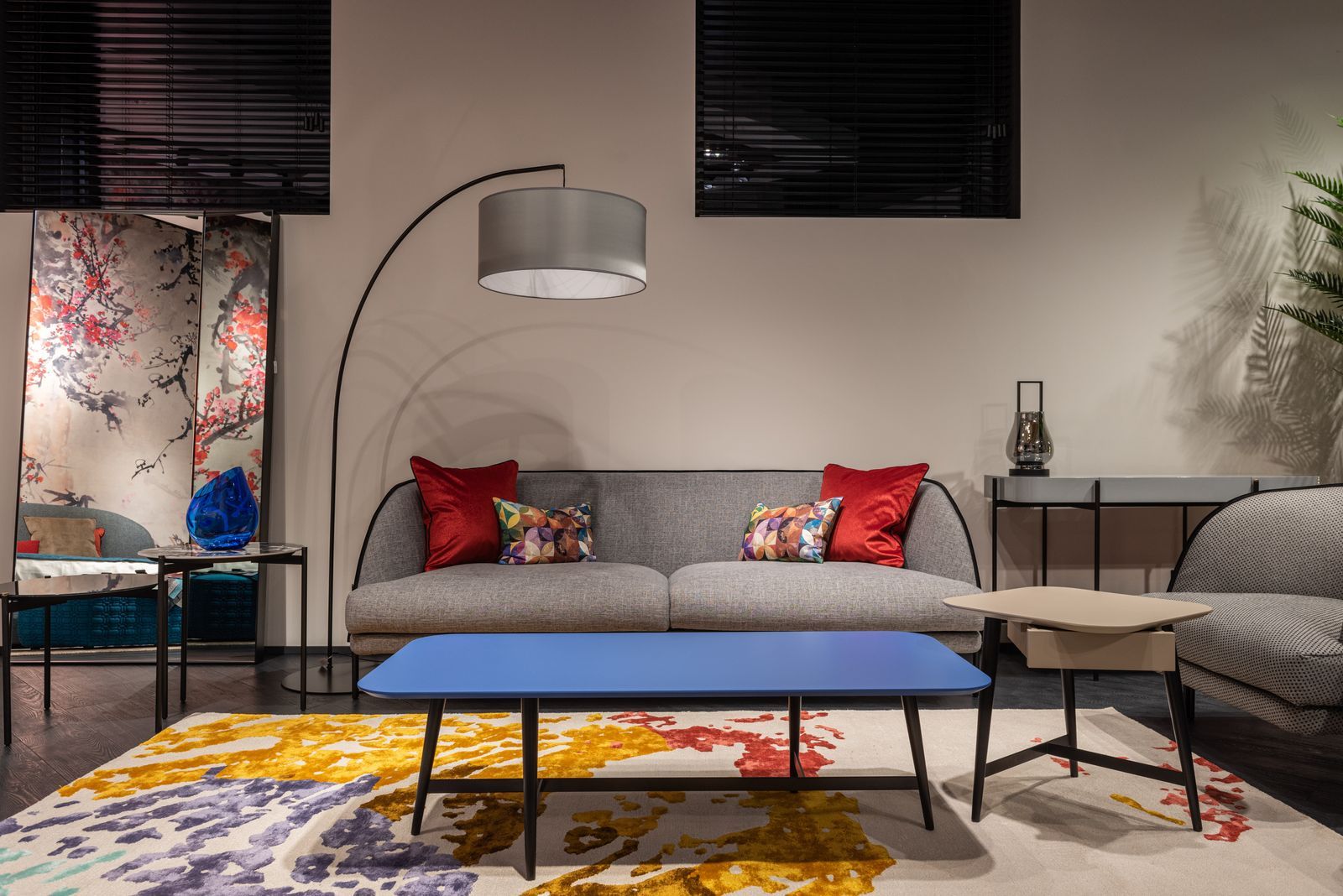 sala de estar d colores neutros con detalles multicolores, cojines rojos, mesita azul, sofá gris