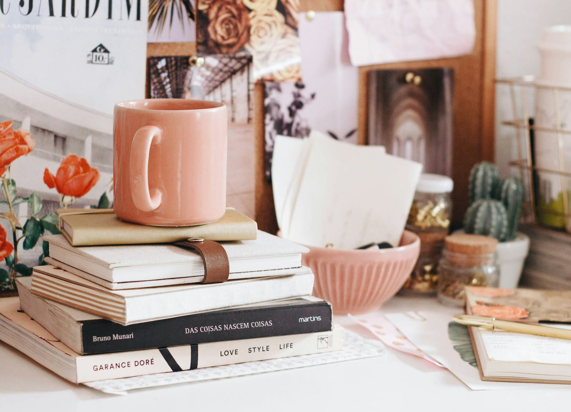 rosafarbenes Dekor mit Büchern, Notizbüchern, einer Punk-Tasse und einigen Bildern auf einem Schreibtisch