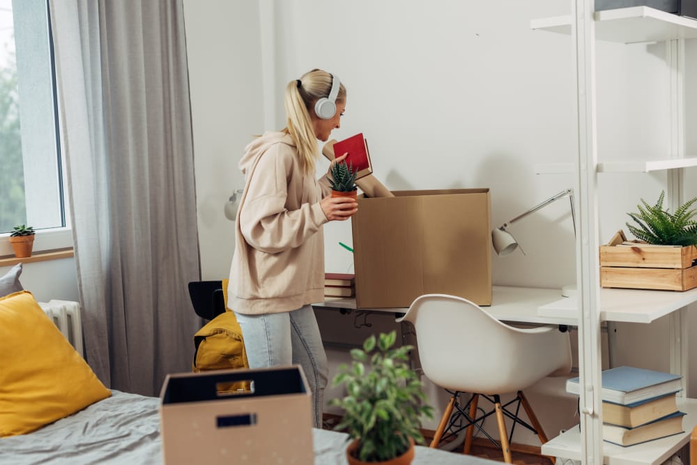 Une étudiante déballe ses affaires dans une boîte en carton dans sa chambre d'étudiant