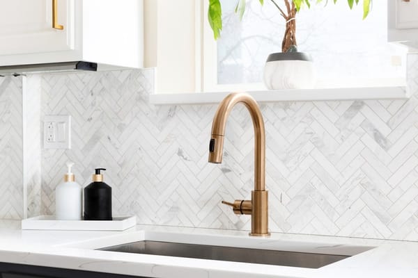 luxury kitchen with herringbone backsplash tiles. white marble countertop, and gold faucet.