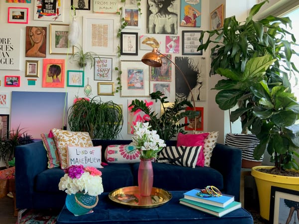 maximalistische Einrichtung mit einem blauen Sofa, vielen Kissen und Wandbildern, Pflanzen